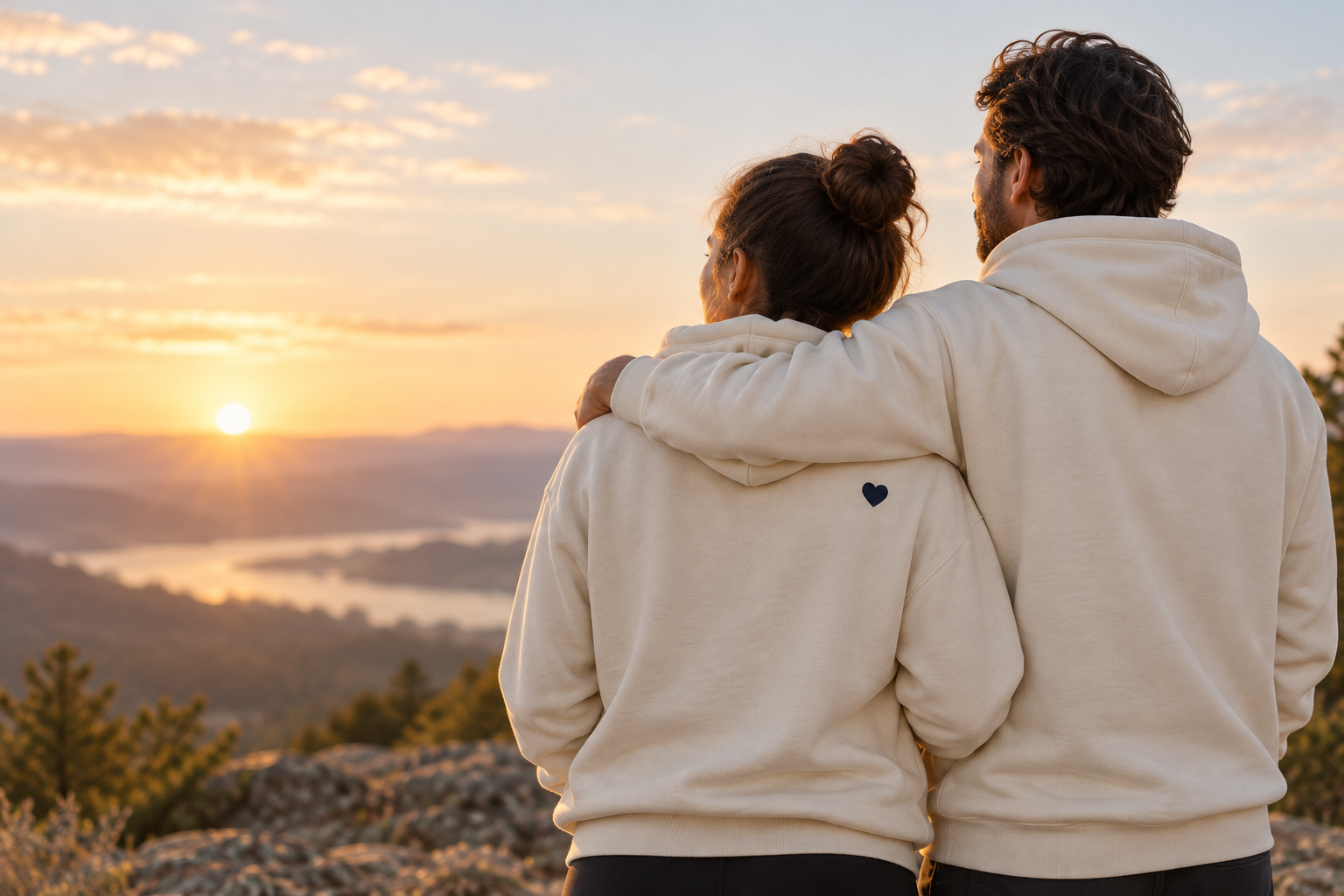 Two people in cream hoodies standing together at sunrise